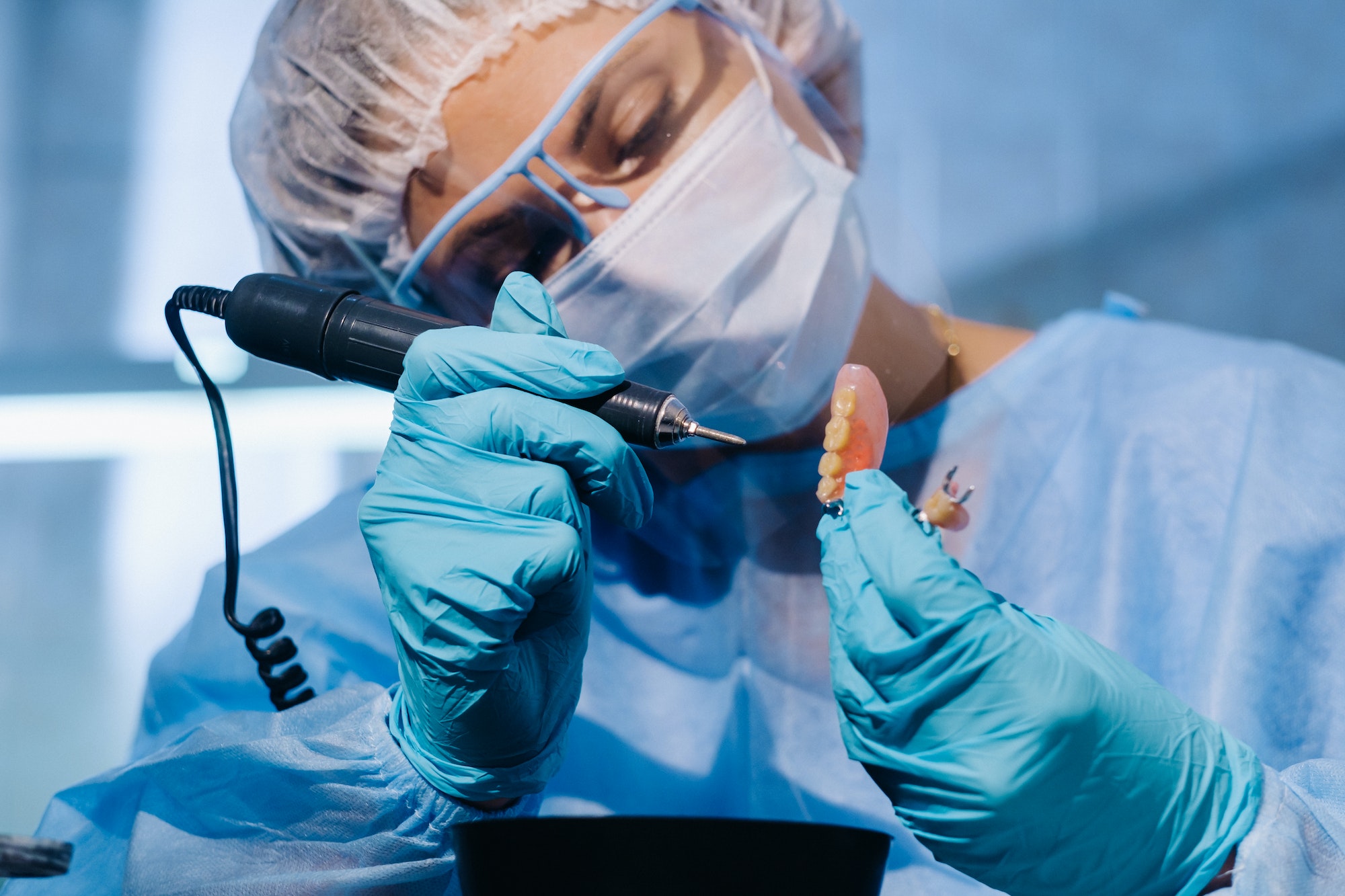 A dental technician in protective clothing is working on a prosthetic tooth in his laboratory