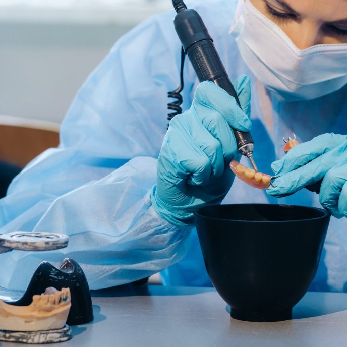 A dental technician in protective clothing is working on a prosthetic tooth in his laboratory
